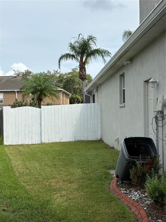 A side yard features a white wooden fence, a palm tree, and a trash bin — 10761 BANFIELD DRIVE, RIVERVIEW, FL