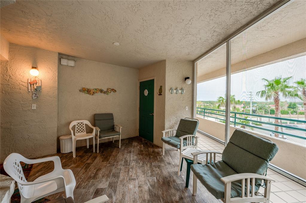A screened-in balcony features tile flooring, several chairs, and a view of palm trees outside — 4575 S ATLANTIC AVENUE UNIT 6310, PORT ORANGE, FL