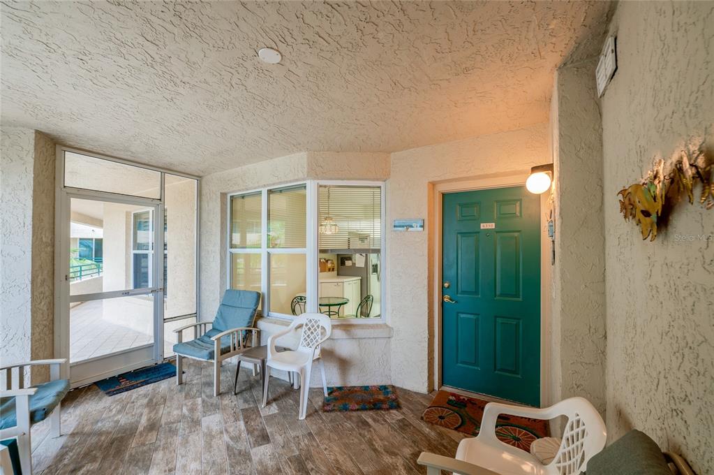 A covered patio with tiled flooring, a teal entrance door, and several chairs — 4575 S ATLANTIC AVENUE UNIT 6310, PORT ORANGE, FL
