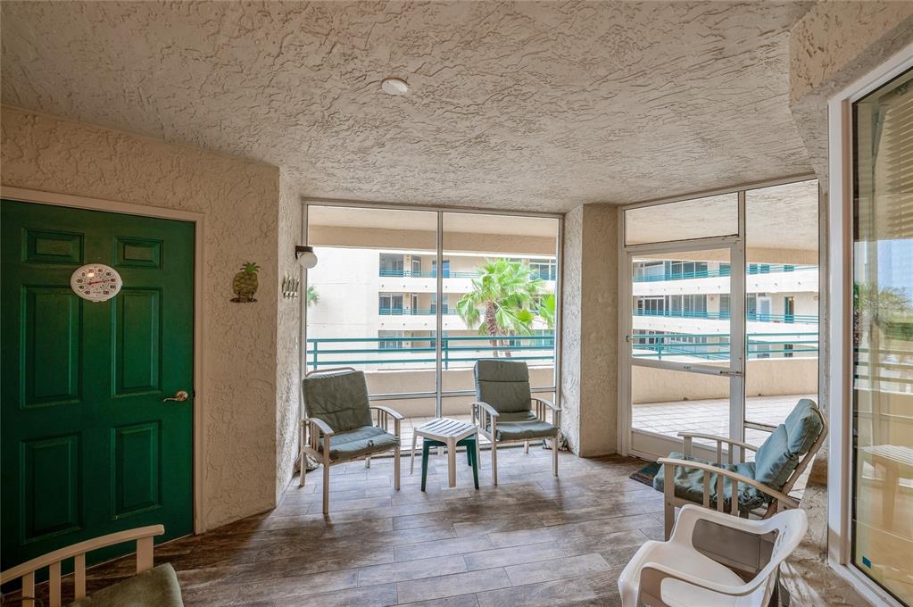 A screened-in balcony features tile flooring, outdoor seating, and a view of a neighboring building — 4575 S ATLANTIC AVENUE UNIT 6310, PORT ORANGE, FL