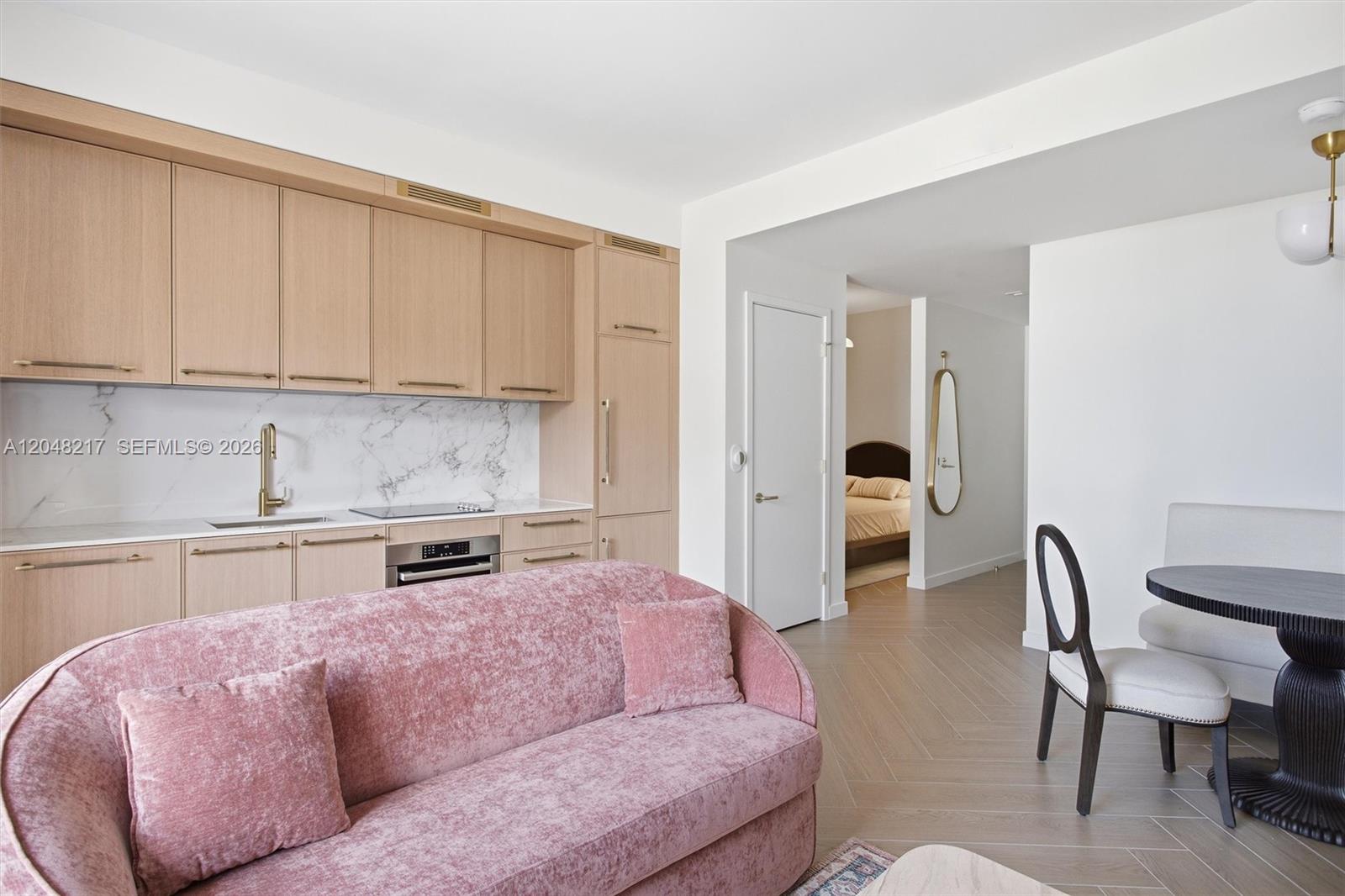A modern kitchen with light wood cabinets and a pink sofa in the foreground — 2700 NW 2nd Ave # 432, Miami FL 33127, MIAMI, FL