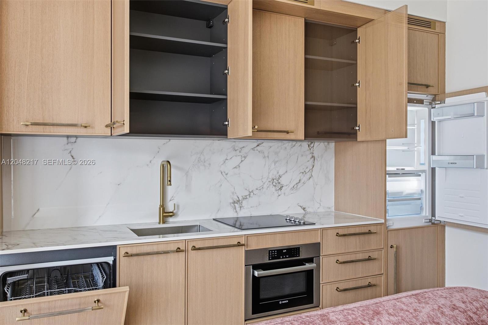A modern kitchen features light wood cabinets, marble countertops, a gold faucet, and integrated appliances — 2700 NW 2nd Ave # 432, Miami FL 33127, MIAMI, FL