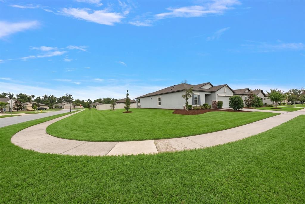 A single-story house with a gray exterior sits on a corner lot with green grass — 13120 CONQUISTADOR LOOP, SPRING HILL, FL