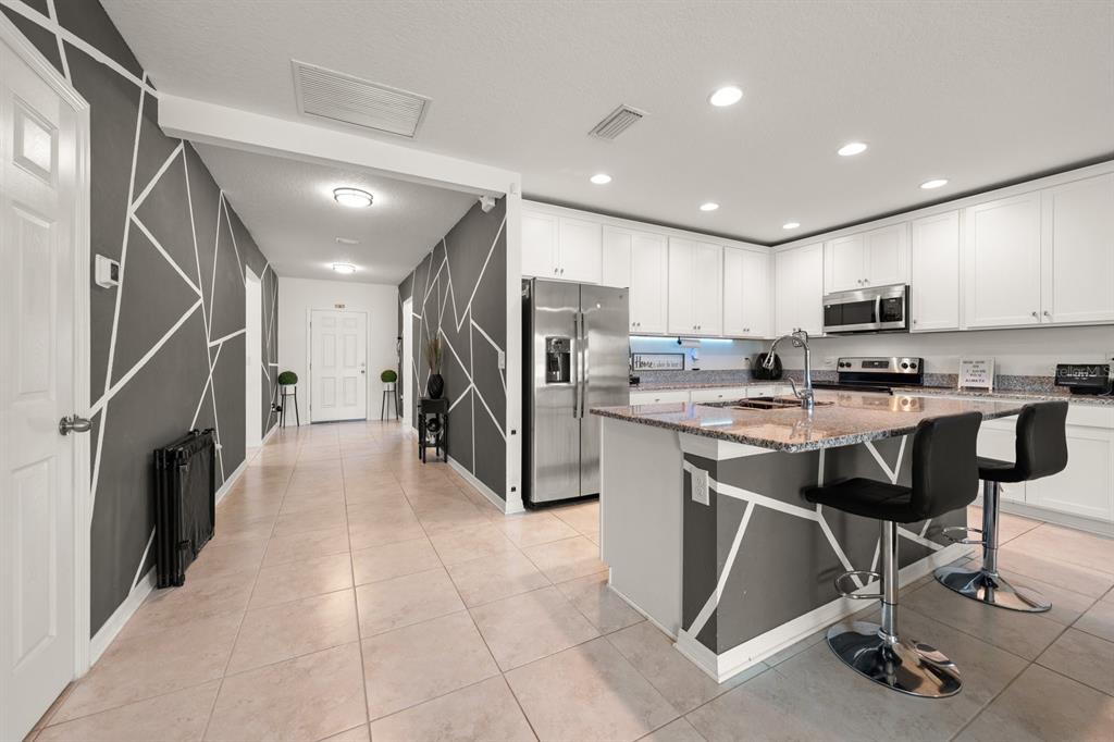 A modern kitchen features white cabinets, granite countertops, and walls with a geometric accent pattern — 13120 CONQUISTADOR LOOP, SPRING HILL, FL