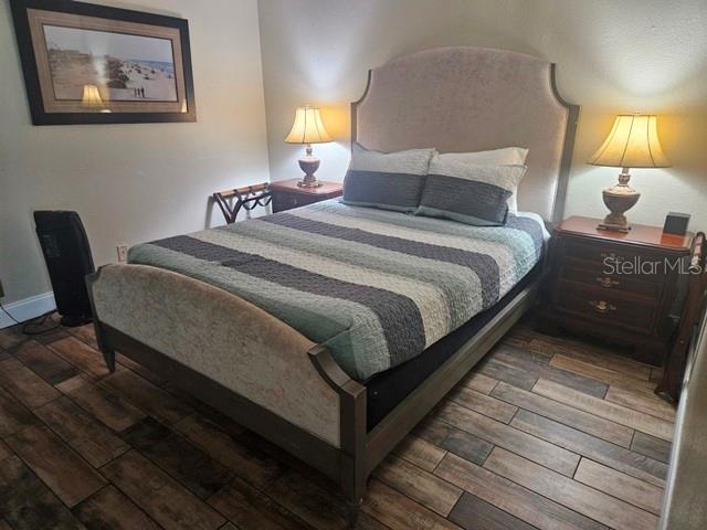 A bedroom features a bed with a striped quilt, two nightstands with lamps, and wood-look flooring — 1909 S ATLANTIC AVENUE UNIT 102, DAYTONA BEACH, FL