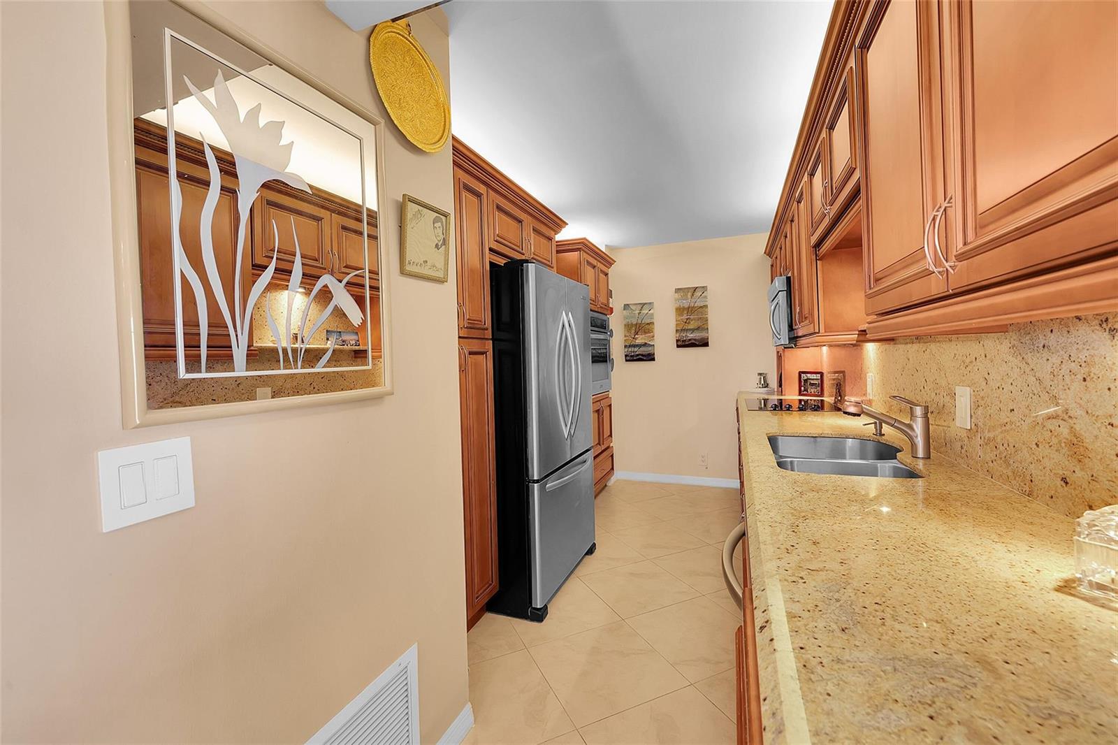 A galley kitchen features wood cabinets, granite countertops, a stainless steel refrigerator, and tile flooring — 1200 Hibiscus Avenue, Pompano Beach FL 33062, POMPANO BEACH, FL