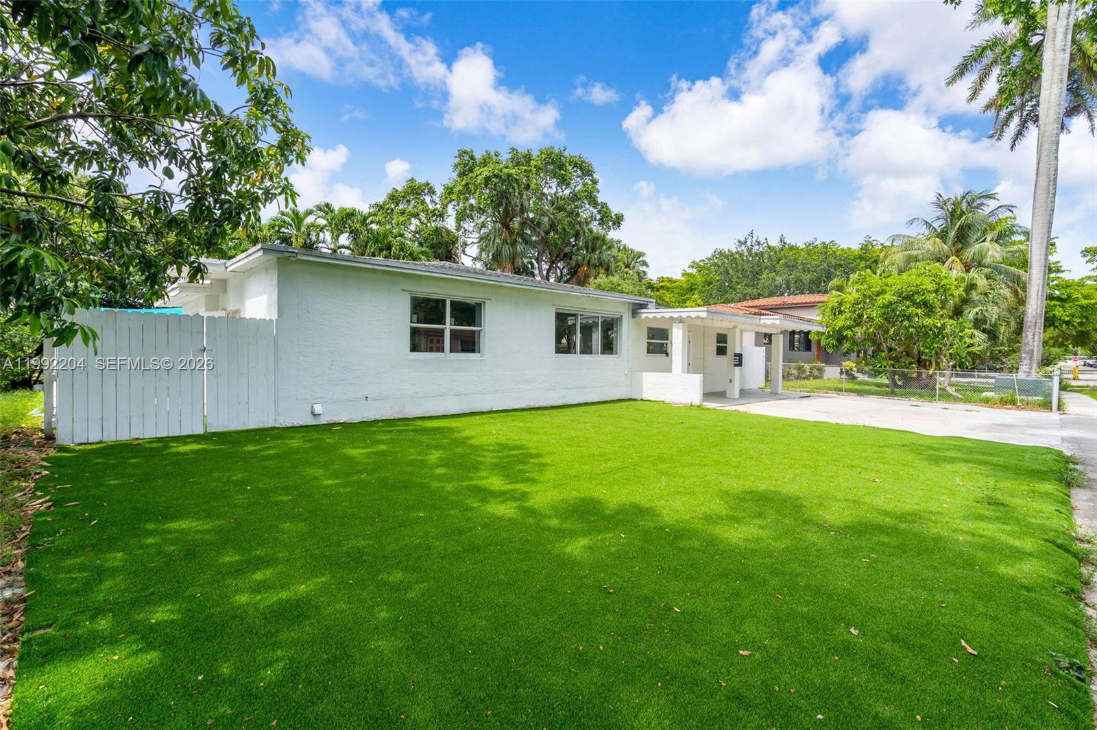 A white single-story house features a green lawn, a white fence, and a palm tree — 181 NE 121st St, North Miami FL 33161, NORTH MIAMI, FL