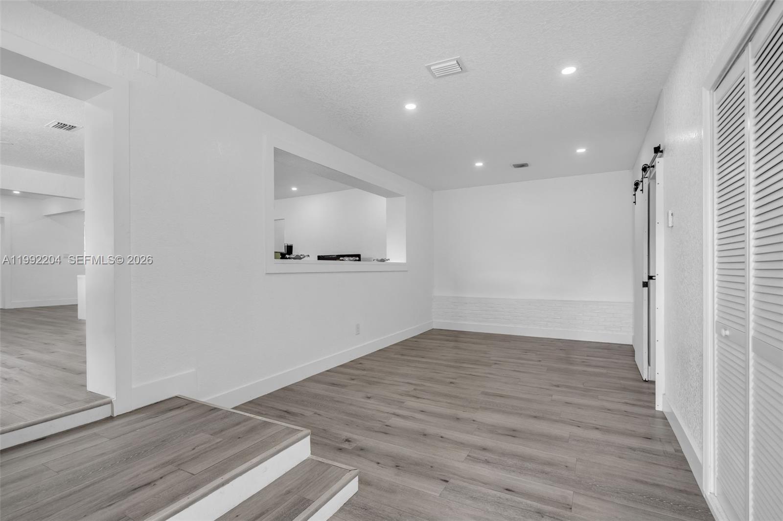 An interior room features white walls, recessed lighting, wood-look flooring, and a pass-through window — 181 NE 121st St, North Miami FL 33161, NORTH MIAMI, FL