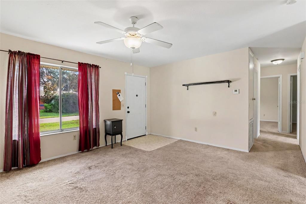 A carpeted living room features a white front door, a ceiling fan, and red curtains — 1610 OMEGA STREET NE, PALM BAY, FL