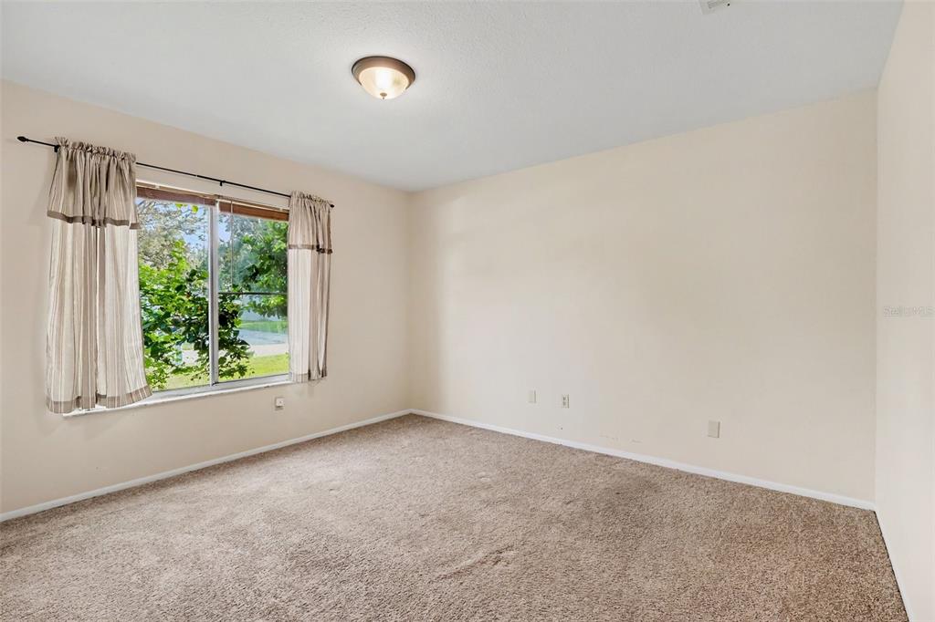 An empty bedroom features beige walls, brown carpeting, a ceiling light, and a window with curtains — 1610 OMEGA STREET NE, PALM BAY, FL