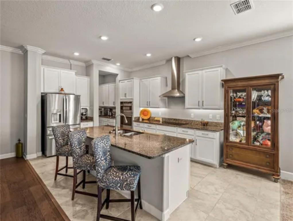 A kitchen features white cabinets, granite countertops, a center island with bar stools, and appliances — 16959 SCUBA CREST STREET, WIMAUMA, FL