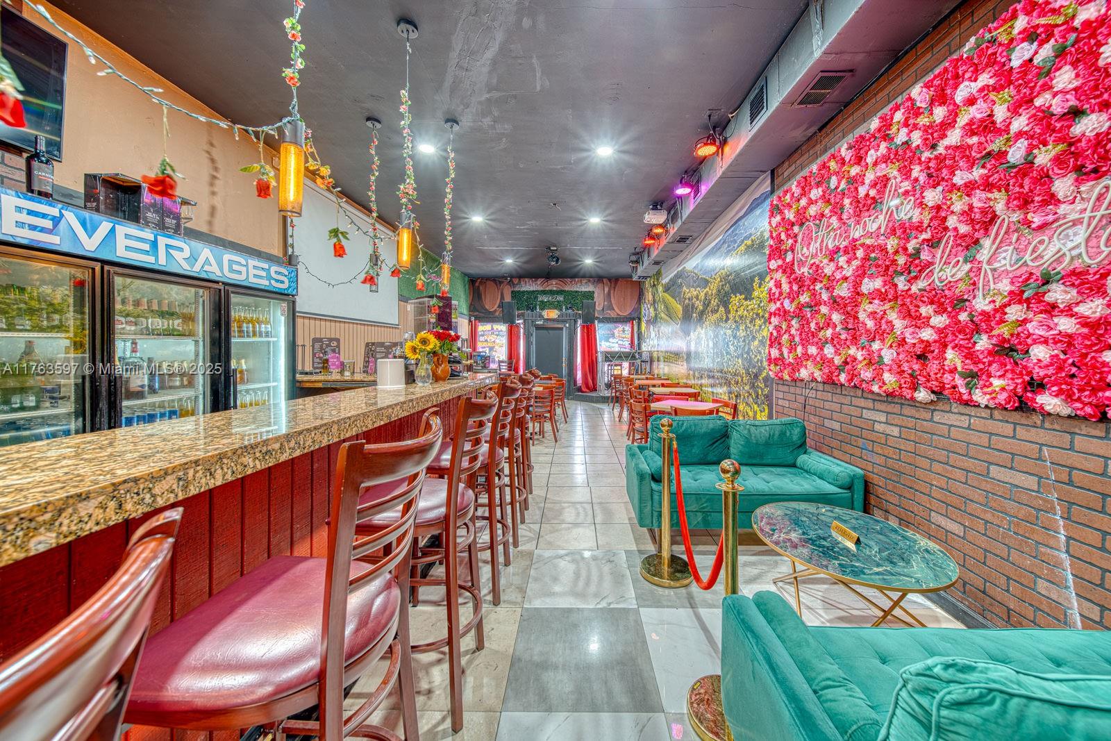 A bar interior features a granite counter, bar stools, green velvet sofas, and floral wall decor — HIGHLY PROFITABLE Restaurant-Bar For Sale on 8th St, Miami FL 33144, MIAMI, FL