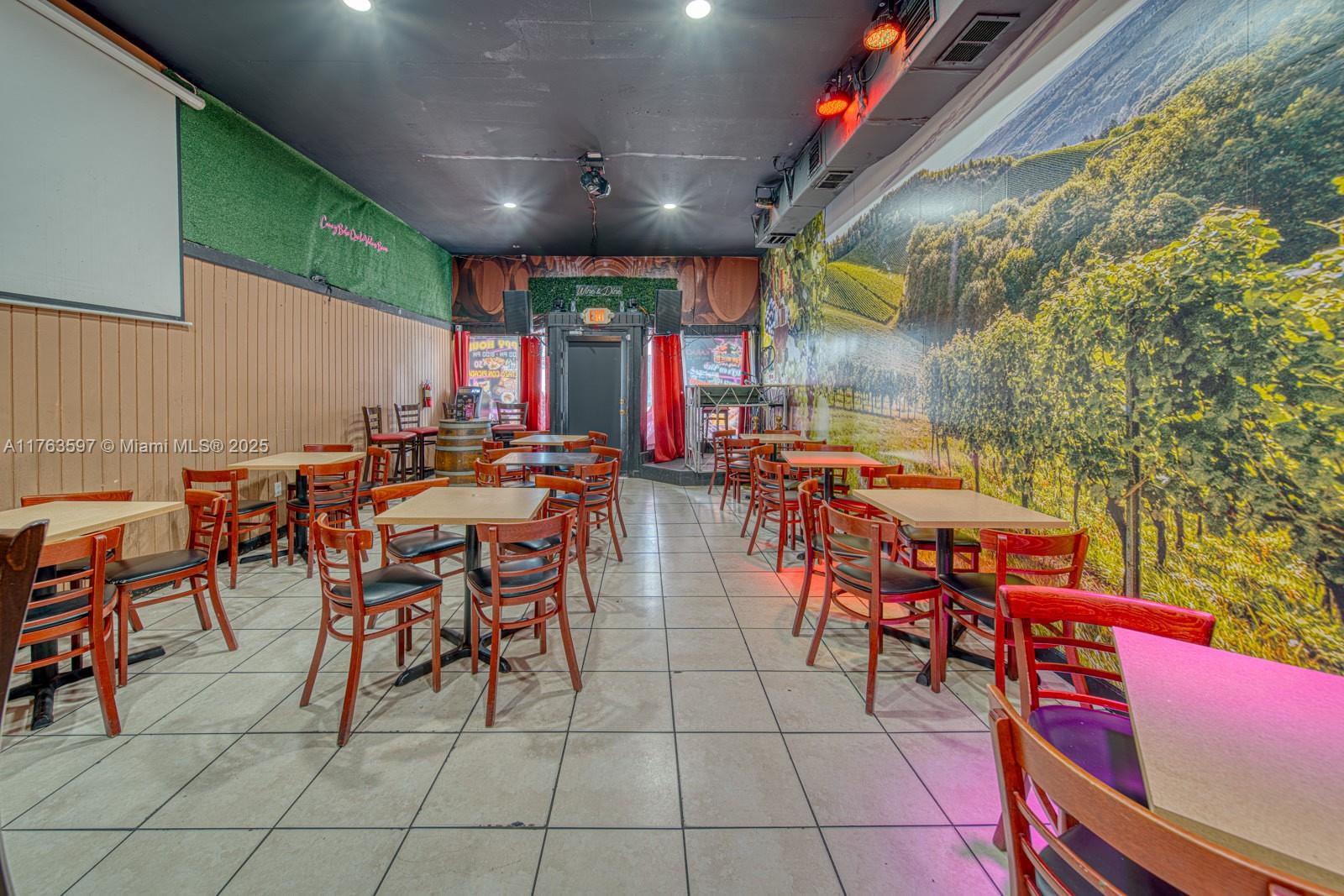 A restaurant interior features tiled floors, wooden chairs, square tables, and a large vineyard wall mural — HIGHLY PROFITABLE Restaurant-Bar For Sale on 8th St, Miami FL 33144, MIAMI, FL