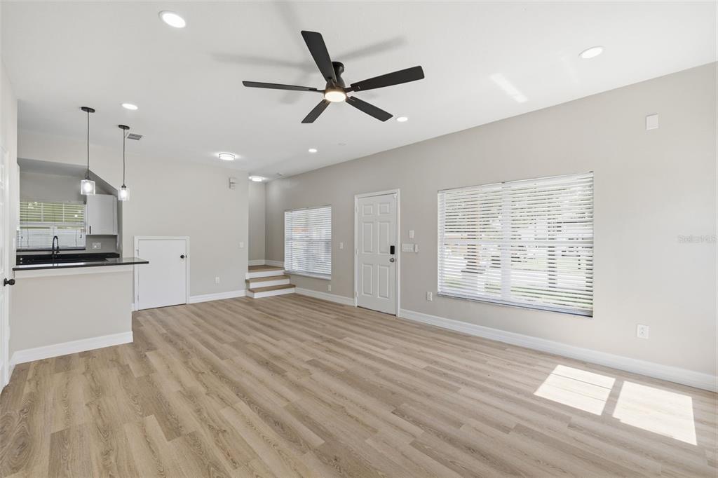 A living room with light wood-look flooring, a ceiling fan, and a kitchen counter area — 319 E HANLON STREET, TAMPA, FL