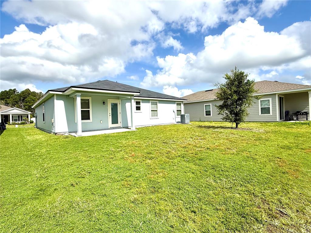 The rear exterior of a light blue house features a covered patio and grassy yard — 1127 GRAND CYPRESS COURT, JACKSONVILLE, FL