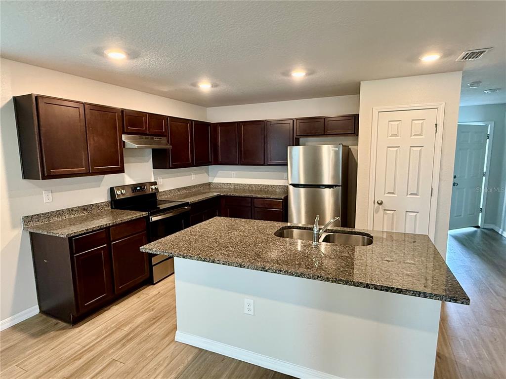 A kitchen features dark wood cabinets, granite countertops, stainless steel appliances, and a central island — 1127 GRAND CYPRESS COURT, JACKSONVILLE, FL
