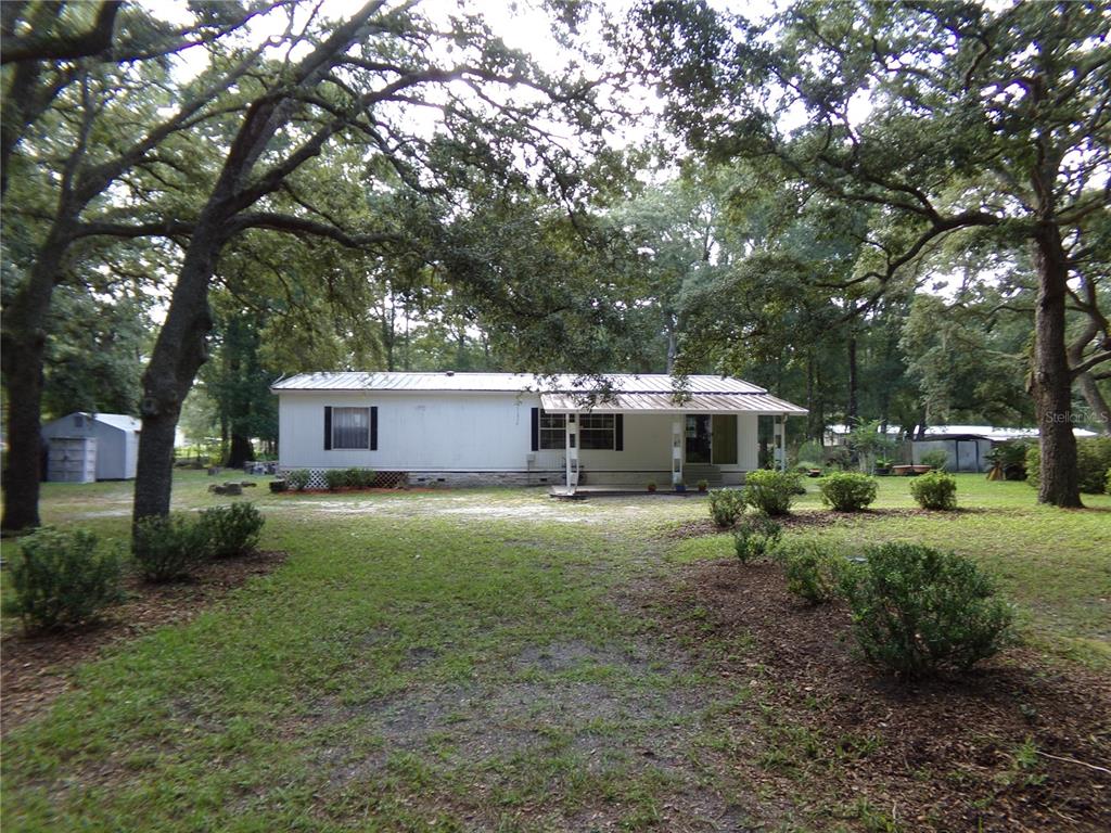 A white single-wide mobile home sits on a grassy lot surrounded by large oak trees — 12199 SW 44TH DRIVE, WEBSTER, FL