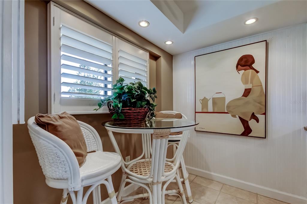 A small breakfast nook features a glass-topped table, two white wicker chairs, and wall art — 9450 HARBOR GREENS WAY UNIT 301, SEMINOLE, FL