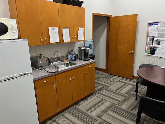 A small office kitchenette features wooden cabinets, a sink, a refrigerator, and a round table — 4965 SW 91ST TERRACE UNIT A, GAINESVILLE, FL