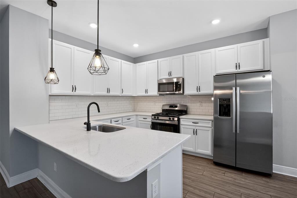 A kitchen with white cabinets, stainless steel appliances, a quartz island, and a subway tile backsplash — 8131 TEA OLIVE TERRACE, PALMETTO, FL