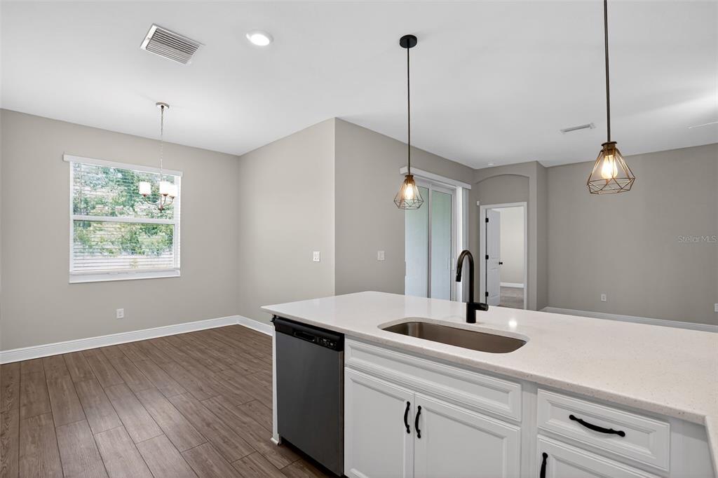 A kitchen island with a sink and pendant lights overlooks a dining area with wood flooring — 8131 TEA OLIVE TERRACE, PALMETTO, FL