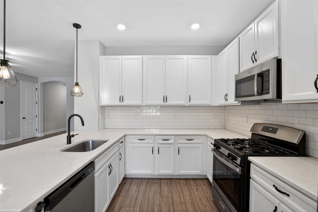 A kitchen with white cabinets, stainless steel appliances, a subway tile backsplash, and wood flooring — 8131 TEA OLIVE TERRACE, PALMETTO, FL