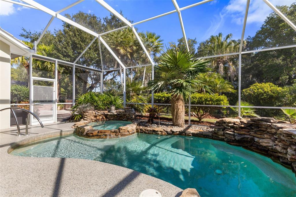 A screened-in pool area features a rock-lined spa, waterfall, and surrounding tropical landscaping — 46 OLD OAK DRIVE S, PALM COAST, FL