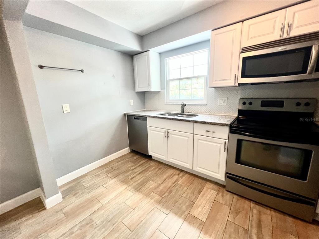 A kitchen features white cabinets, stainless steel appliances, a window, and wood-look tile flooring — 14402 REUTER STRASSE CIRCLE UNIT 223, TAMPA, FL