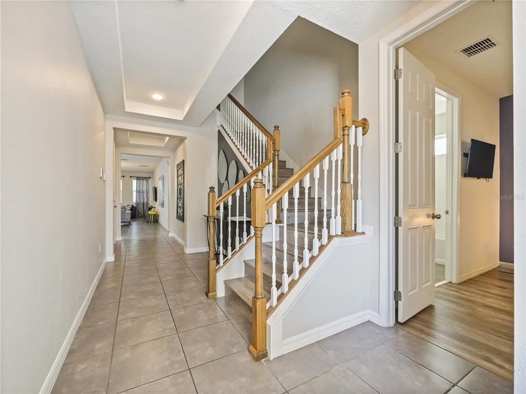 A foyer features a tiled floor, a wooden staircase with white railings, and an open doorway — 1810 SAWYER PALM PLACE, KISSIMMEE, FL