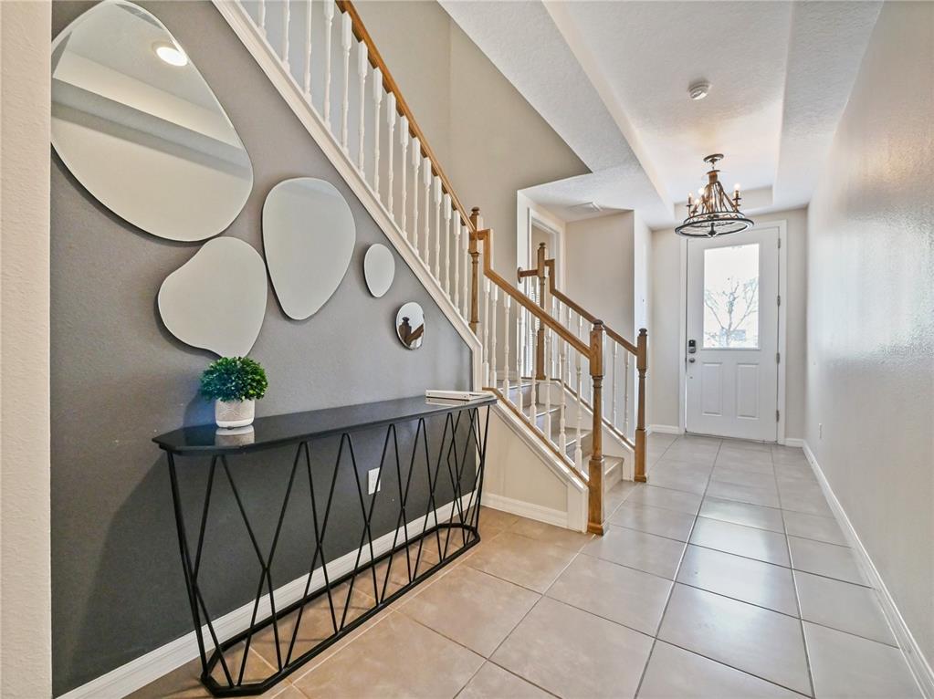 An entryway features a staircase with white railings, a black console table, and wall mirrors — 1810 SAWYER PALM PLACE, KISSIMMEE, FL