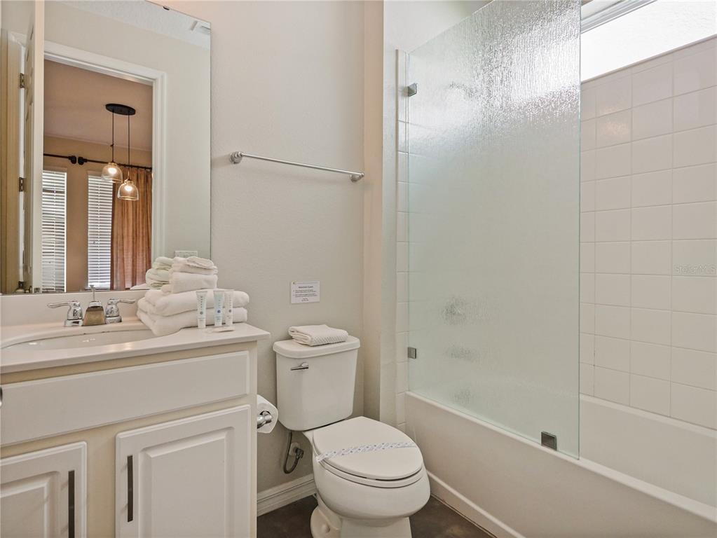A bathroom features a white vanity, a toilet, and a bathtub with a glass shower door — 1810 SAWYER PALM PLACE, KISSIMMEE, FL
