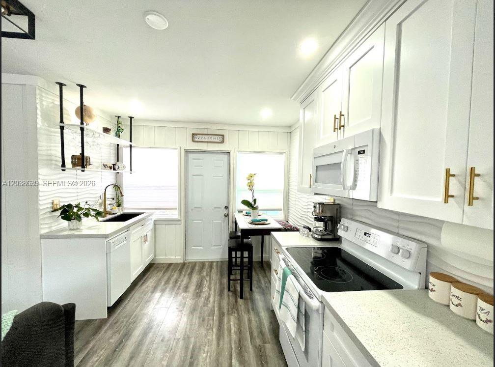 A bright kitchen features white cabinetry, a black stove, wood-look flooring, and a small dining area — 1218 N 24th Ave, Hollywood FL 33020, HOLLYWOOD, FL
