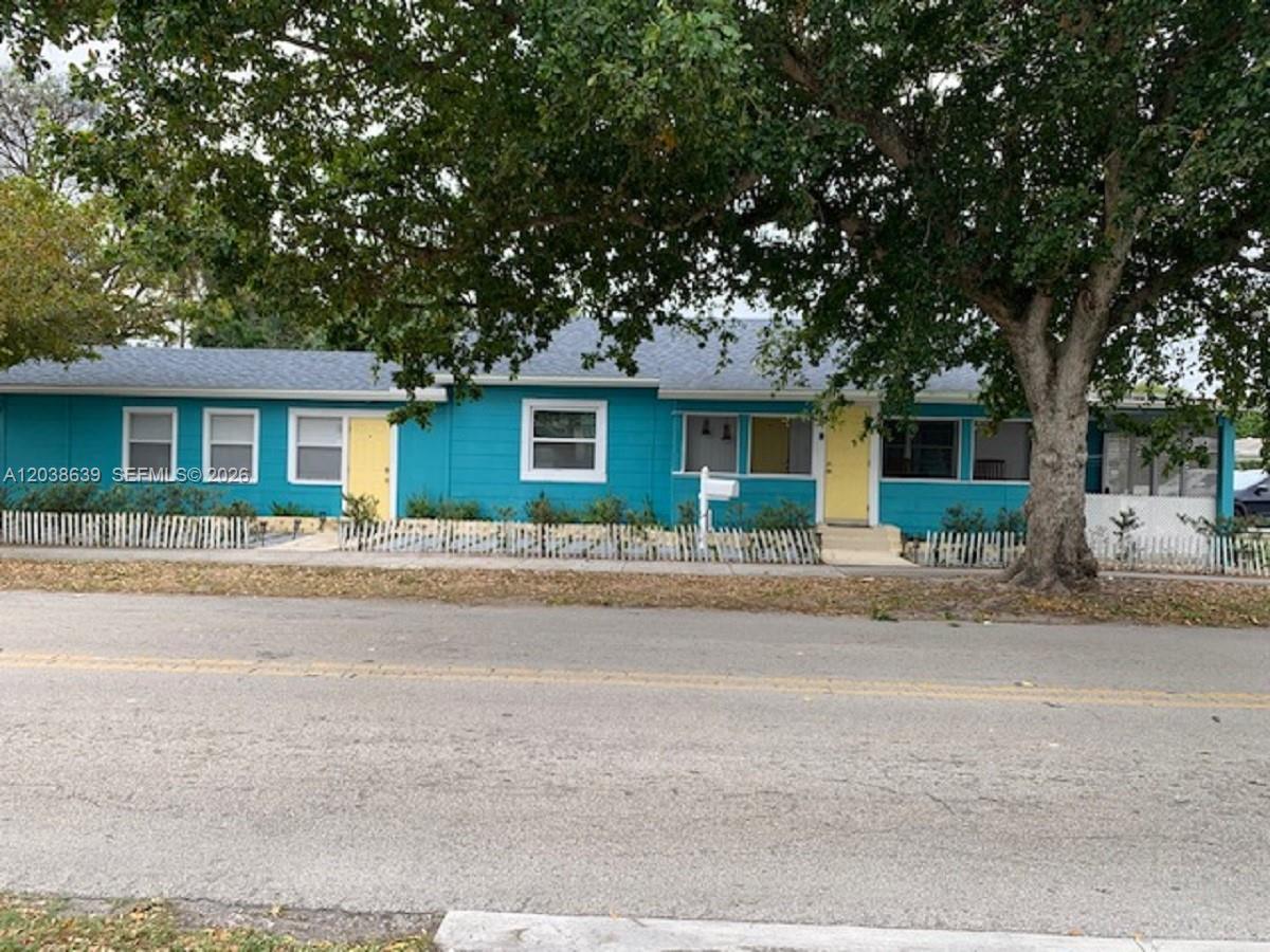 A single-story teal house with yellow doors and a white picket fence under large trees — 1218 N 24th Ave, Hollywood FL 33020, HOLLYWOOD, FL