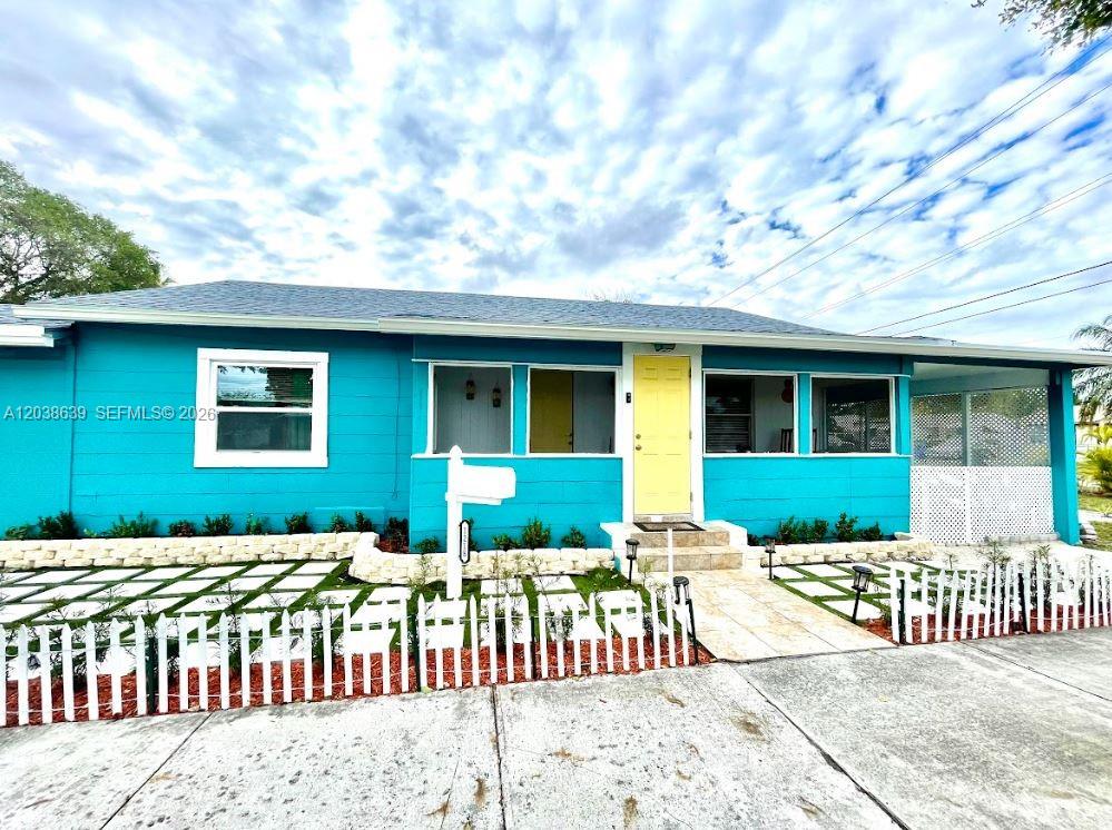A bright blue single-story house features a yellow front door and a white picket fence — 1218 N 24th Ave, Hollywood FL 33020, HOLLYWOOD, FL
