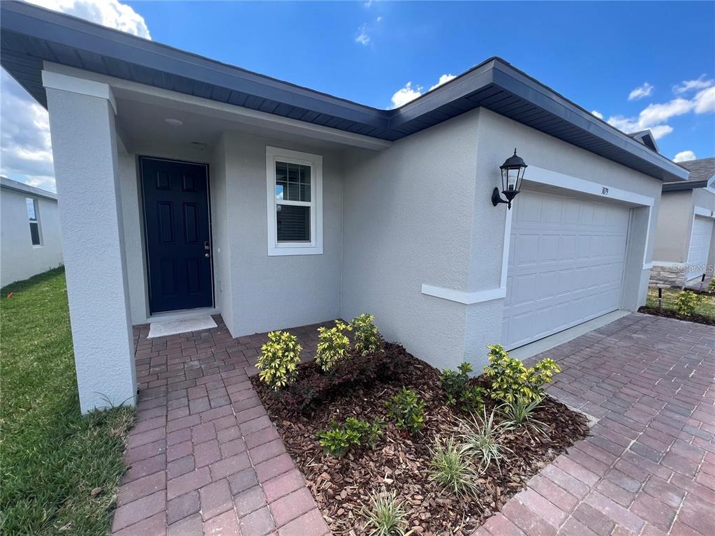 A single-story house exterior features a dark blue front door, a garage, and landscaping — 3079 LAUREL OAK LANE, WINTER HAVEN, FL