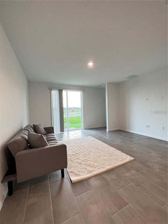 A living room with tile flooring, a gray sofa, a rug, and sliding glass doors — 3079 LAUREL OAK LANE, WINTER HAVEN, FL
