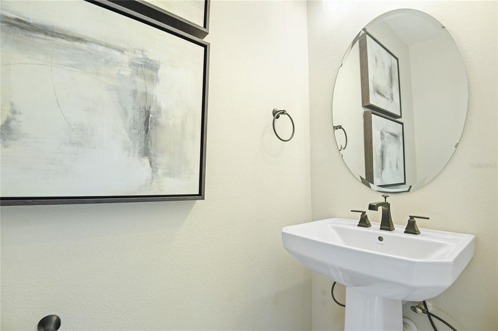 A powder room features a pedestal sink, an oval mirror, and abstract wall art — 6394 CLOVER STREET, LAKE HAMILTON, FL