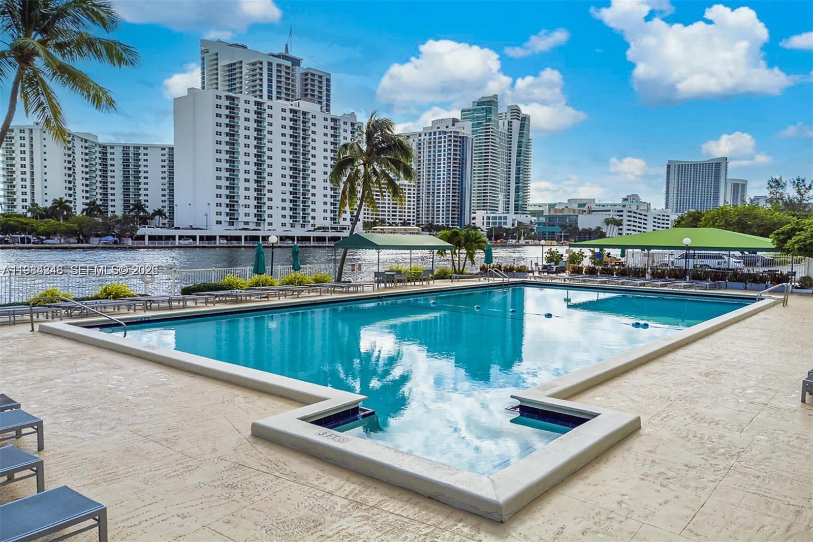 An outdoor swimming pool overlooks a waterway with high-rise buildings in the background — 800 Parkview Dr # 527, Hallandale Beach FL 33009, HALLANDALE BEACH, FL