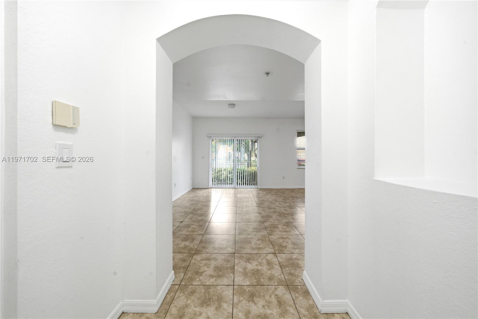 An arched doorway leads into a bright, empty room with tiled floors and sliding glass doors — 8999 NW 107th Ct # 1, Doral FL 33178, DORAL, FL