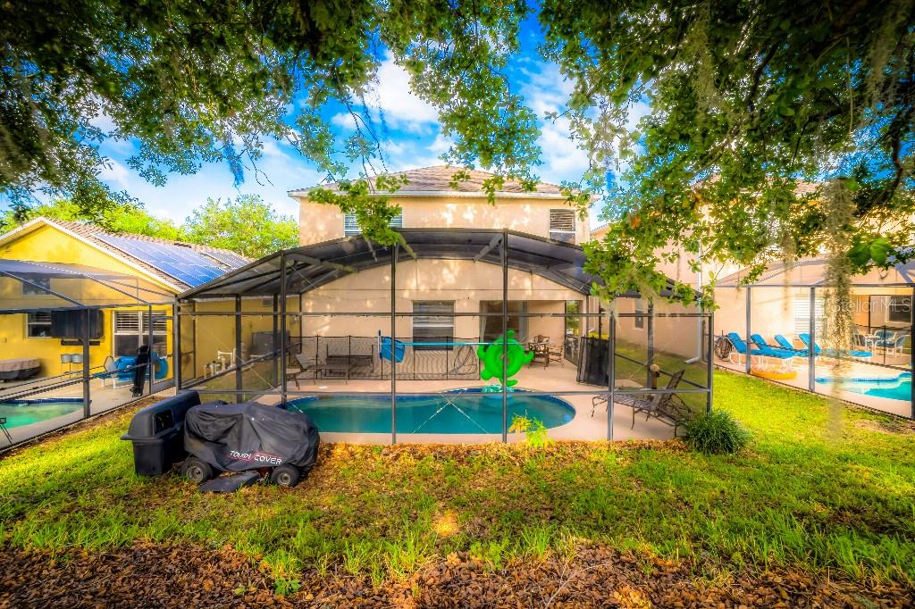 A backyard view of a two-story house featuring a screened-in swimming pool and patio area — 1142 MARINER CAY DRIVE, HAINES CITY, FL