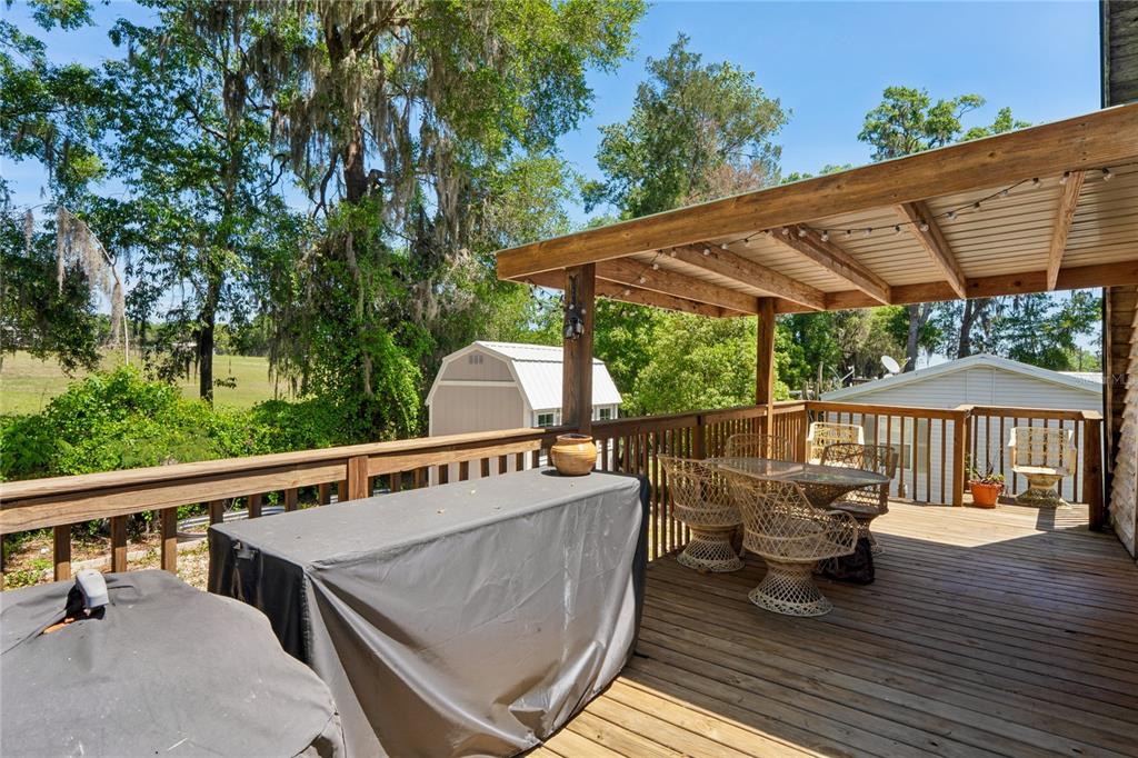 A wooden deck features a covered patio area, wicker furniture, and a grill with covers — 9366 CR 649, BUSHNELL, FL