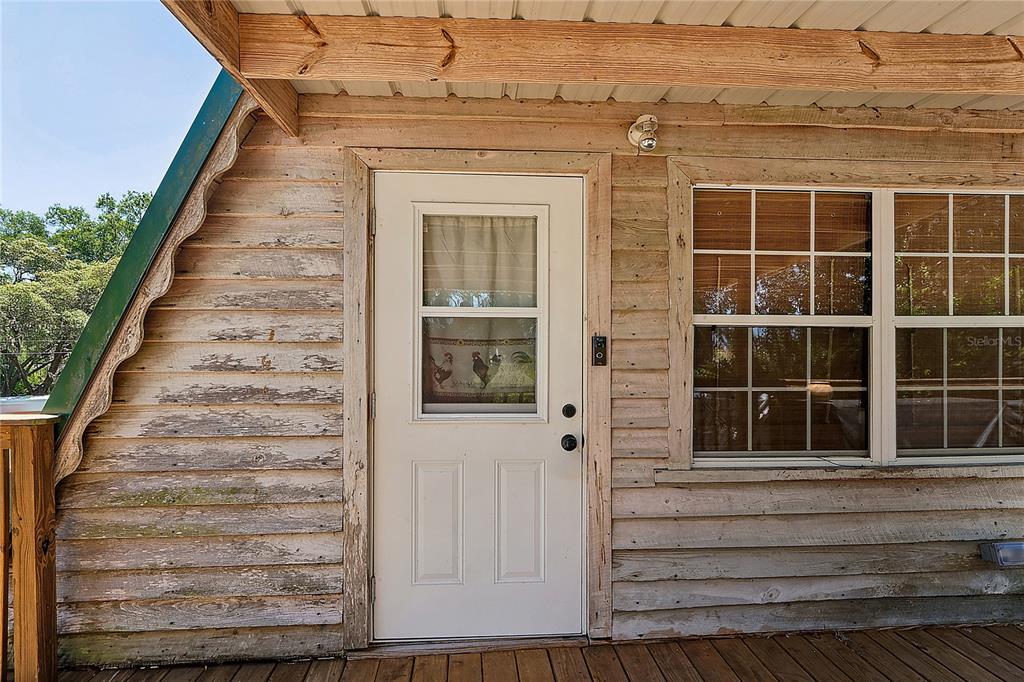 A white exterior door is set into a weathered wood-sided wall on a wooden porch — 9366 CR 649, BUSHNELL, FL
