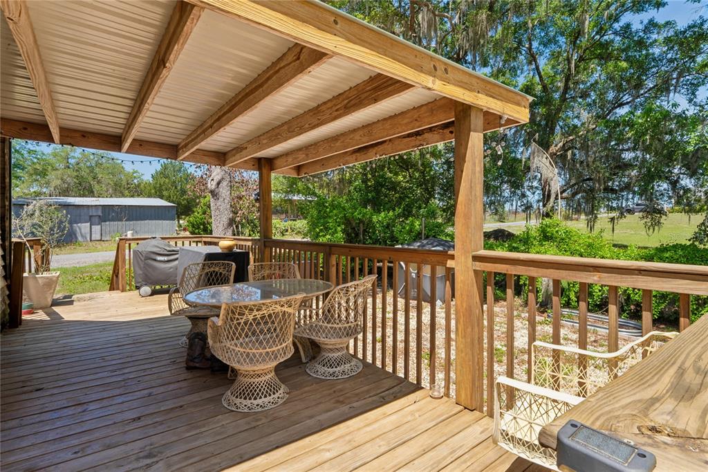 A wooden deck features a covered patio area with a dining set and railing — 9366 CR 649, BUSHNELL, FL