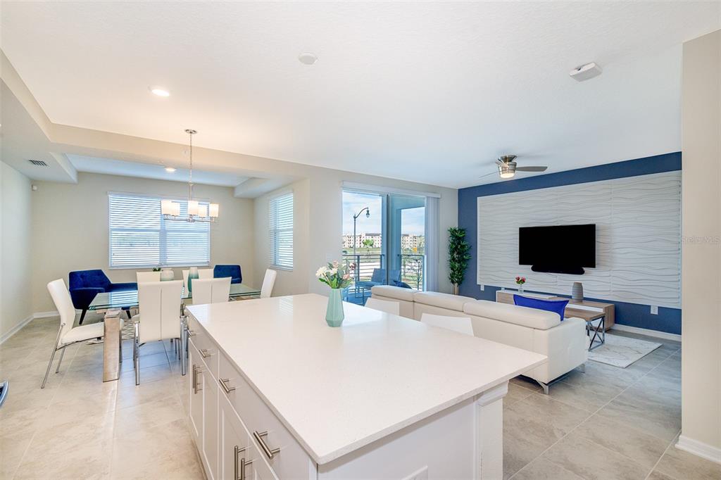 A bright open-concept living and dining area features a kitchen island, tile floors, and balcony — 4731 CLOCK TOWER DRIVE UNIT 206, KISSIMMEE, FL
