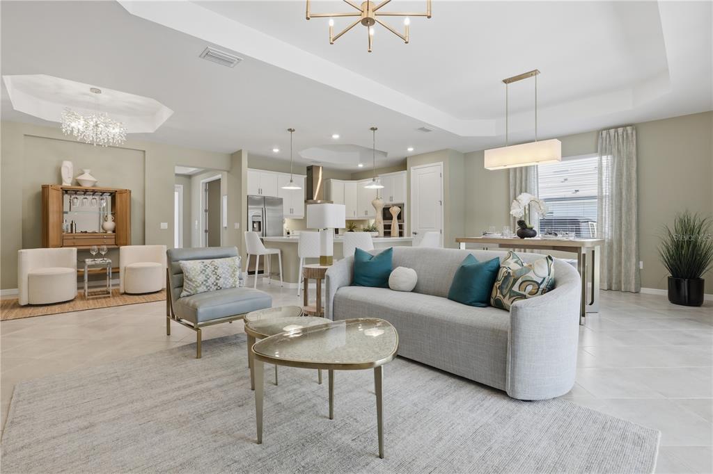 An open-concept living room and kitchen area with light-colored tile floors and modern furniture — 19732 TROUT TERRACE, LAKEWOOD RANCH, FL