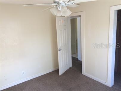 A bedroom with beige walls, brown carpet, a ceiling fan, and two open doorways — 625 HOLMES AVENUE, DAYTONA BEACH, FL
