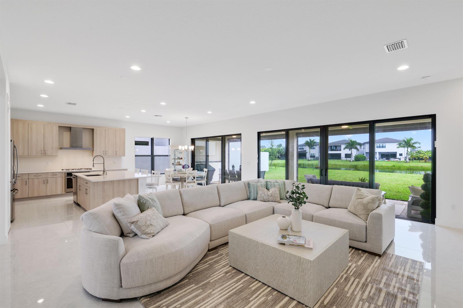 A bright open-concept living room with a large sectional sofa, kitchen, and sliding glass doors — 20028 Pacific Dunes Drive, Boca Raton FL 33434, BOCA RATON, FL