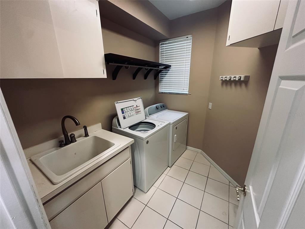 A laundry room features a utility sink, white appliances, tile flooring, and wall-mounted shelving — 3125 STONEWATER DRIVE, LAKELAND, FL