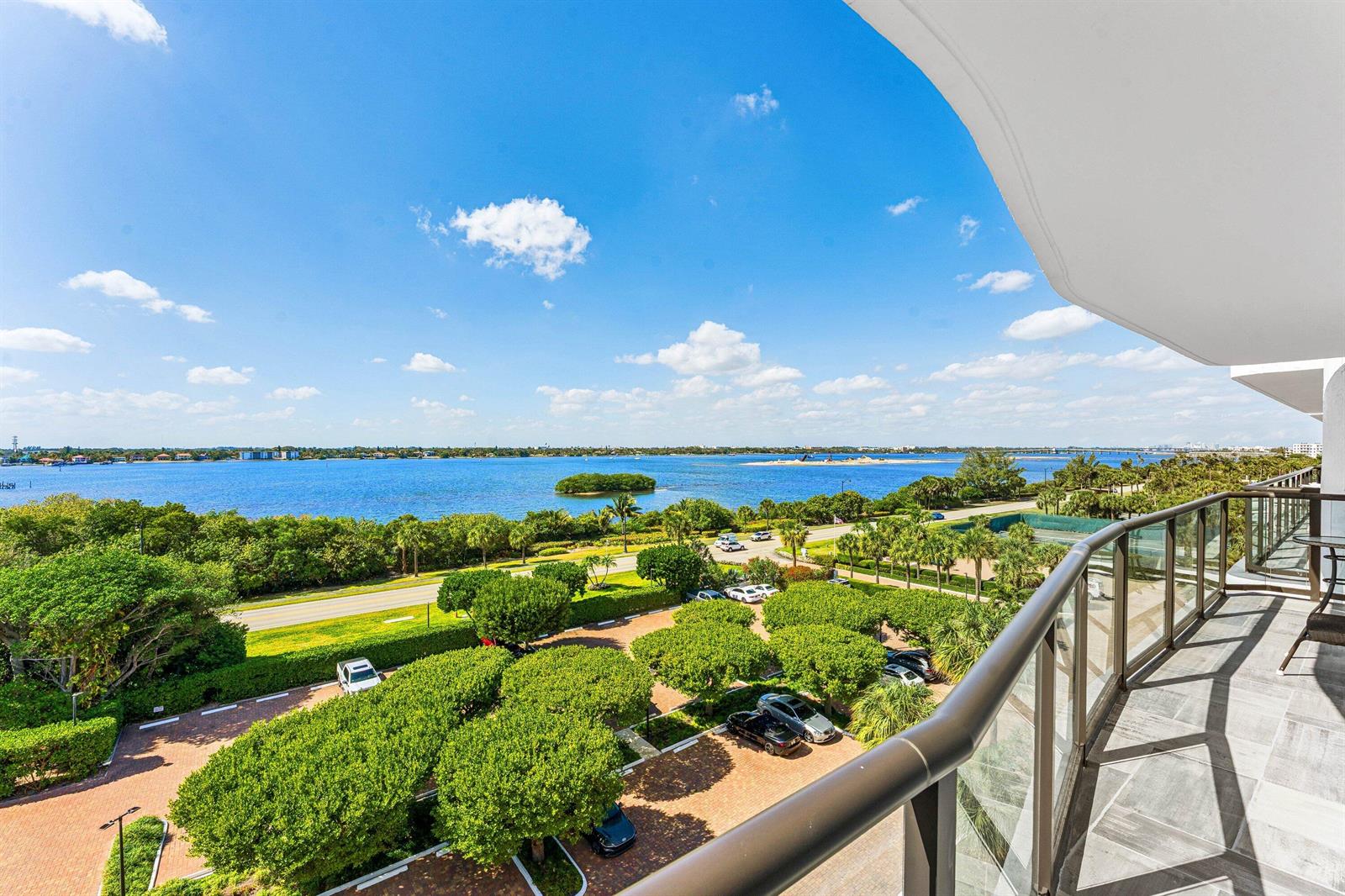 A high-angle view from a balcony overlooking a parking lot, trees, and a large bay — 3440 S Ocean Boulevard NE # 608s, Palm Beach FL 33480, PALM BEACH, FL