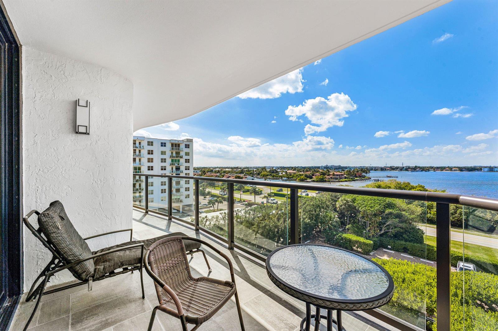 A balcony with a glass railing overlooks a coastal landscape with water and buildings — 3440 S Ocean Boulevard NE # 608s, Palm Beach FL 33480, PALM BEACH, FL